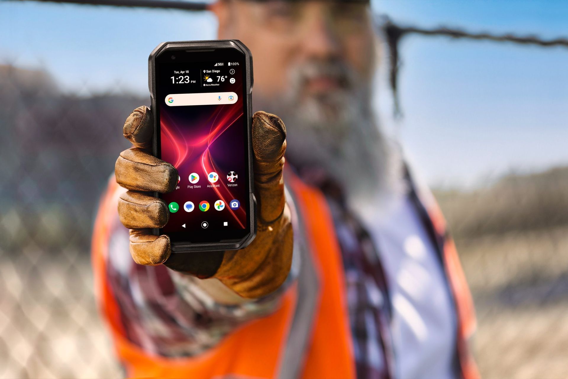 A man in an orange vest is holding a cell phone in his hand.
